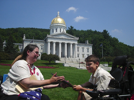 A young man in a wheelchair receives and advocacy award on the Statehouse Lawn.