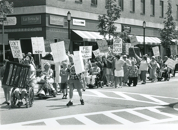 A photo of disability rights protesters marching with signs that read full access for everybody.