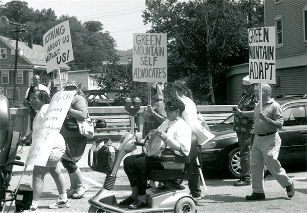 A photograph of advocates carrying signs that read nothing about us without us.