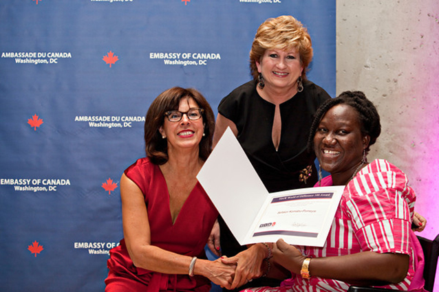 A young woman from Ghana in  wheelchair, with 2 other women accepting a T I A W award.