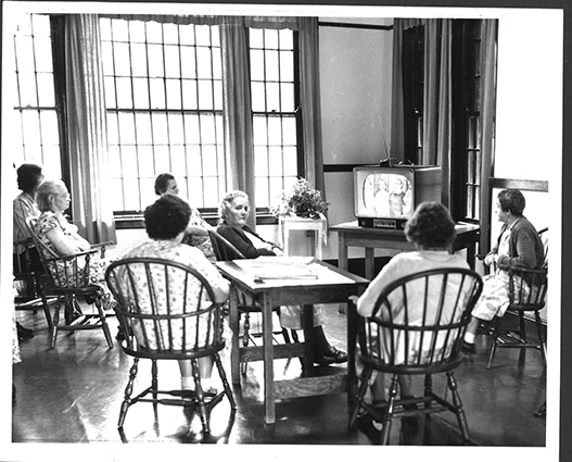 Photograph from 1954 of seven women sitting in a lounge at the state hospital watching TV.