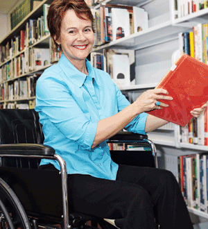 A woman in a wheelchair smiles as she is working in a library