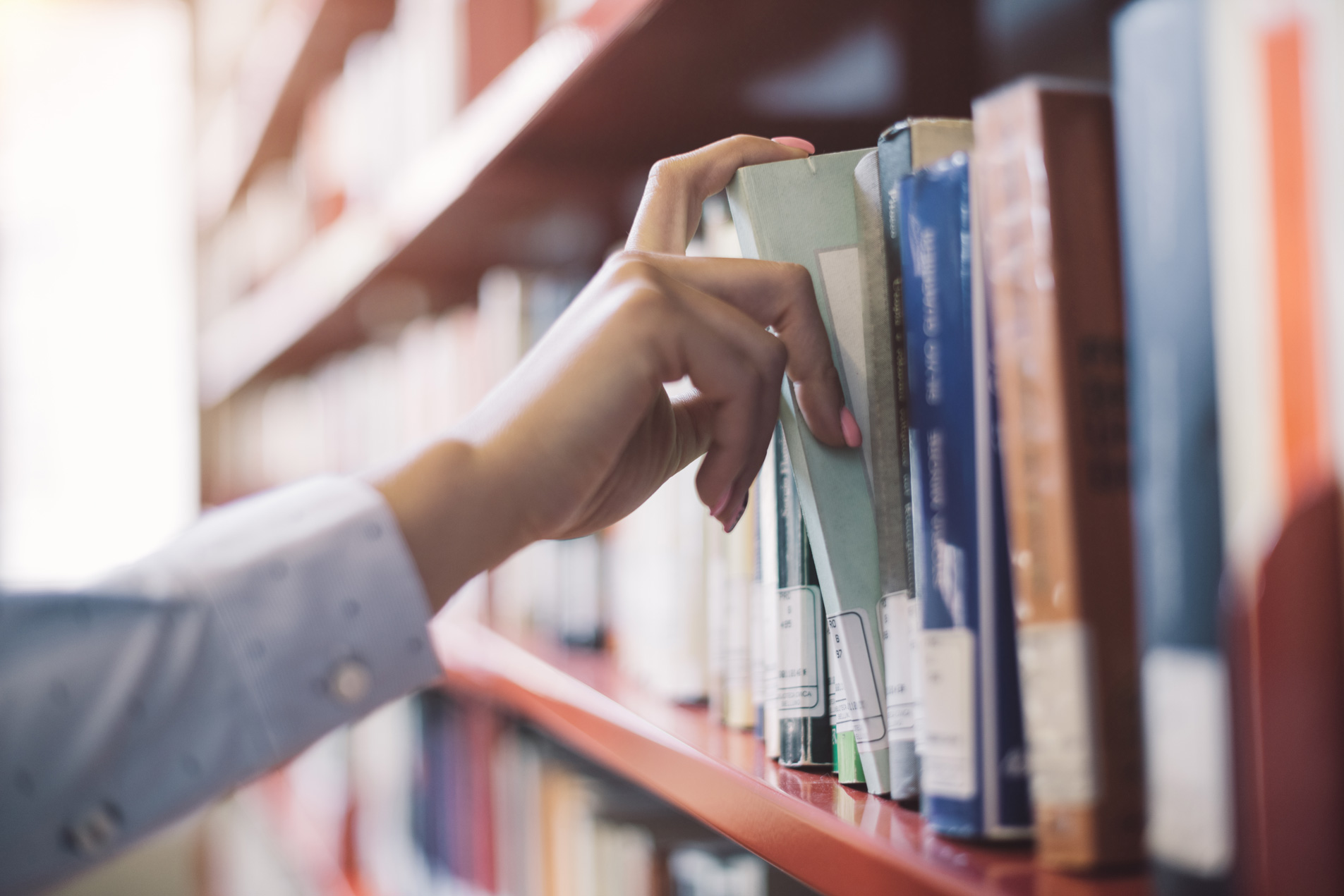A woman's hand in a library pulling a library book off the shelf