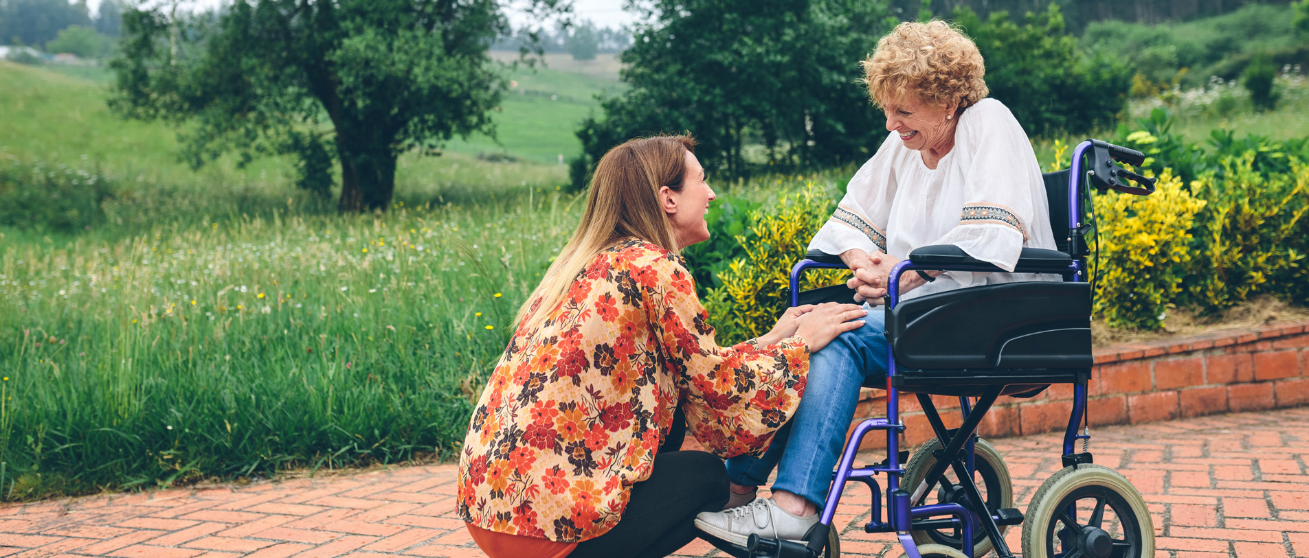 Caregiving crouching down in front of smiling mature woman in a wheelchair